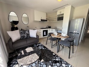 Ein modernes Wohnzimmer mit einer Couch, zwei Sesseln, einem Couchtisch und einem Essbereich mit Tisch und Stühlen.