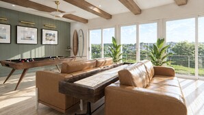 Una mesa de billar con estructura de madera y un sofá de cuero en una habitación con ventanas amplias y vistas al verdor.