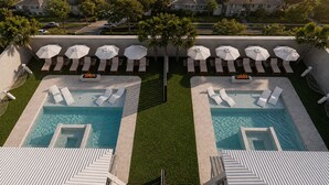 Un área de piscina en la azotea con dos piscinas separadas, cada una rodeada de sillas de descanso y sombrillas.