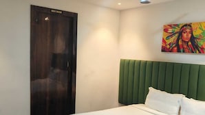 A hotel room with a bed, a green headboard, a painting on the wall, and a sign indicating a rest room.