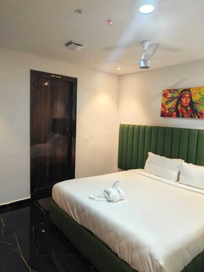 A hotel room with a bed, a green headboard, a painting on the wall, and a sign indicating a rest room.