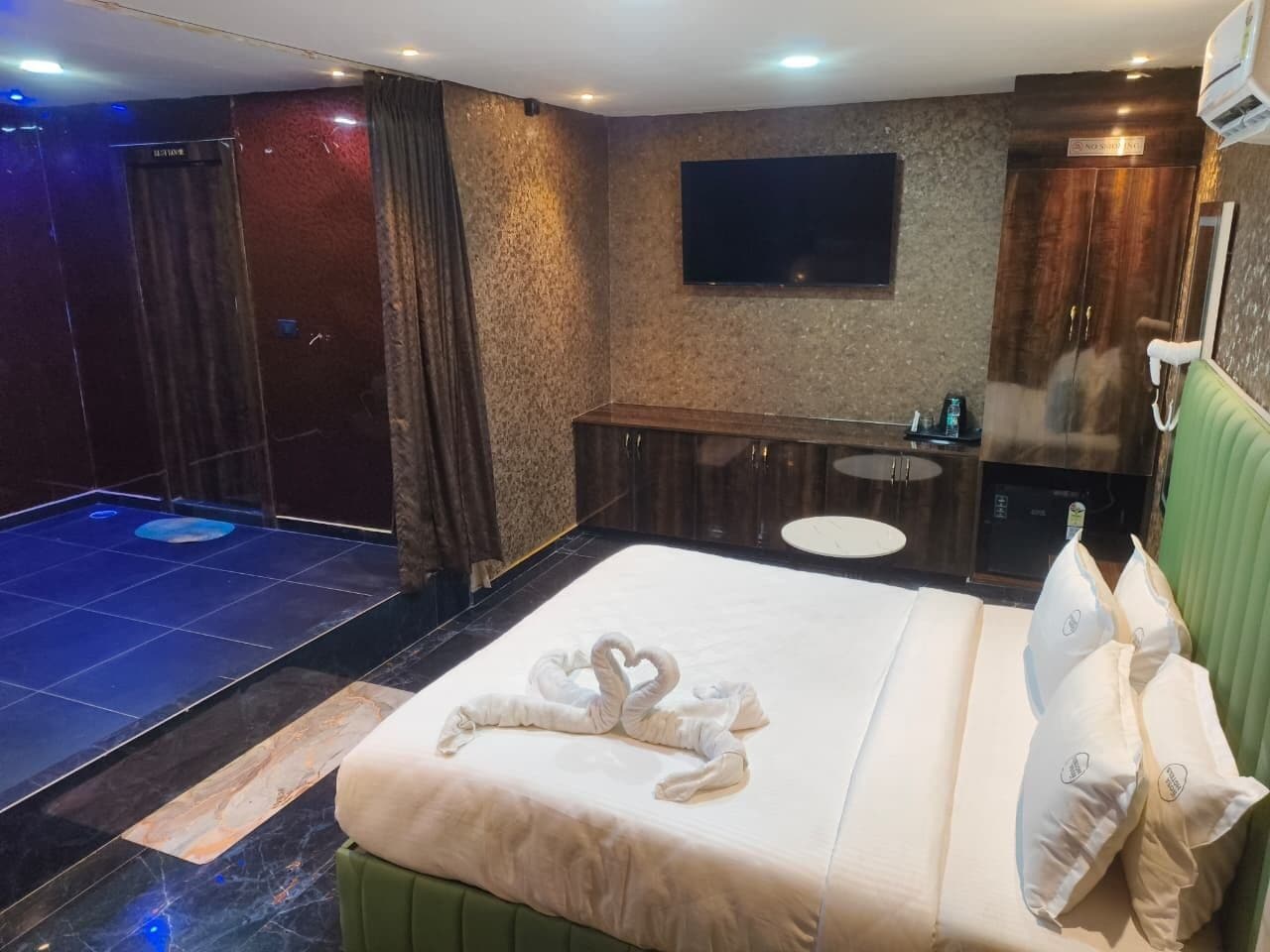 A hotel room with a bed, a small desk, a mirror, and a wall-mounted TV.