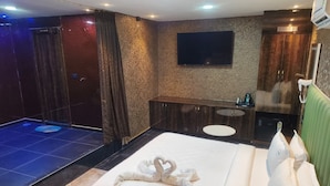 A hotel room with a bed, a small desk, a mirror, and a wall-mounted TV.