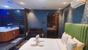 A hotel room with a large bed, a green headboard, a massage chair, and a spa area with a hot tub.