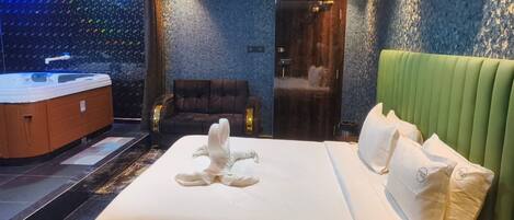 A hotel room with a large bed, a green headboard, a massage chair, and a spa area with a hot tub.
