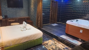 A hotel room with a bed, a sitting area, a hot tub, and a television.