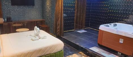 A hotel room with a bed, a sitting area, a hot tub, and a television.