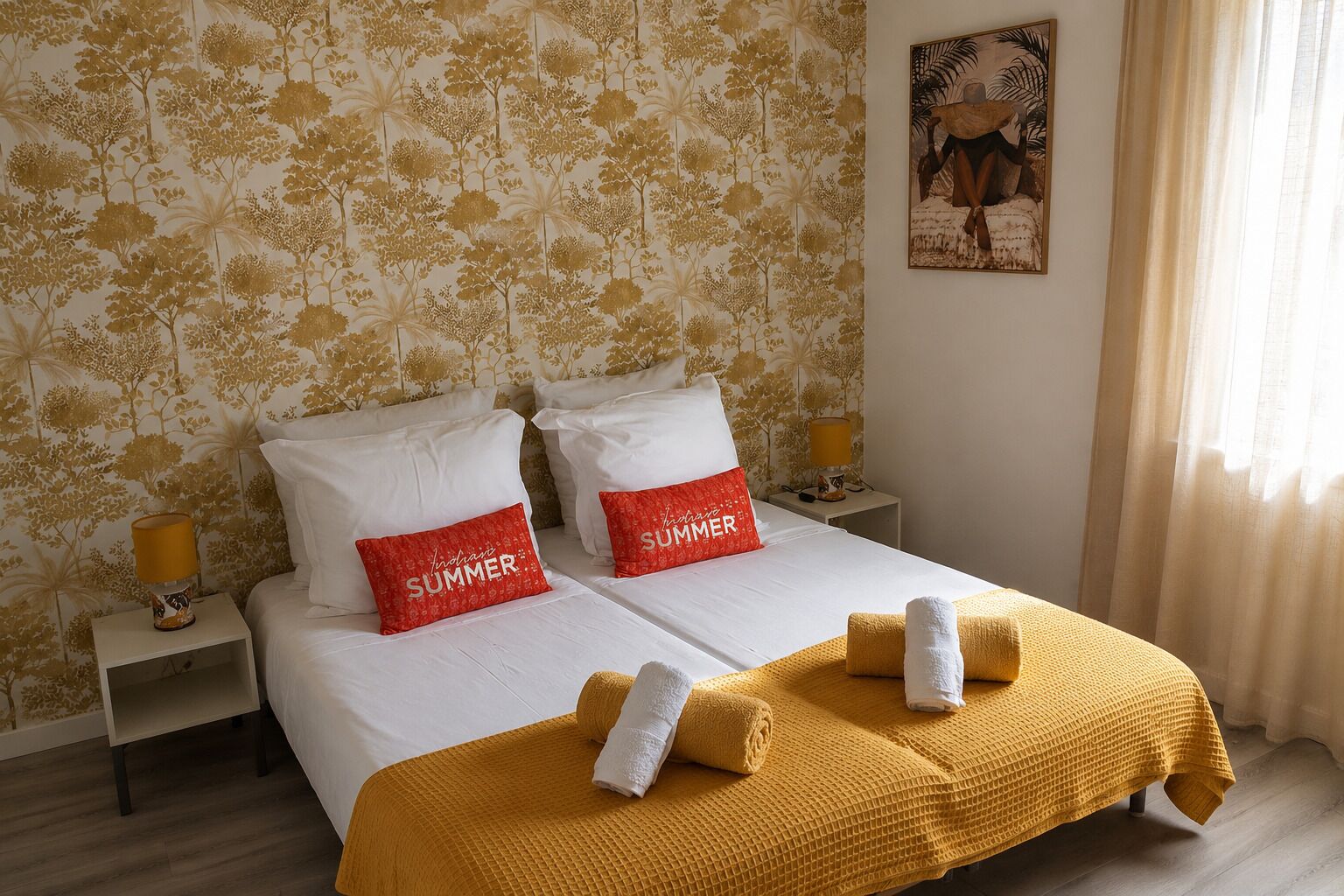 Un lit double avec du linge de lit blanc, deux oreillers rouges ornés de l’inscription « INDIAN SUMMER », un plaid jaune et un tableau accroché au mur.
