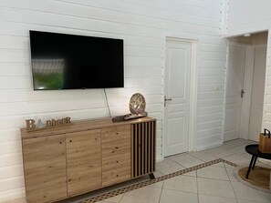 A modern living room with a flat-screen TV mounted on a white wall, a wooden cabinet with drawers, and a decorative item on top. - Villa Ti-Coco with a private pool (Saint-François)