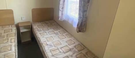 A single-bed room with a window, a bedside table, and a hanging light fixture.