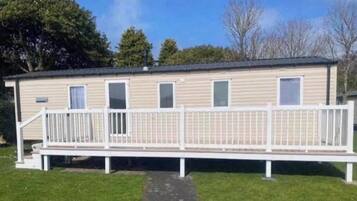 A single-story mobile home with a white porch and a fenced deck area.