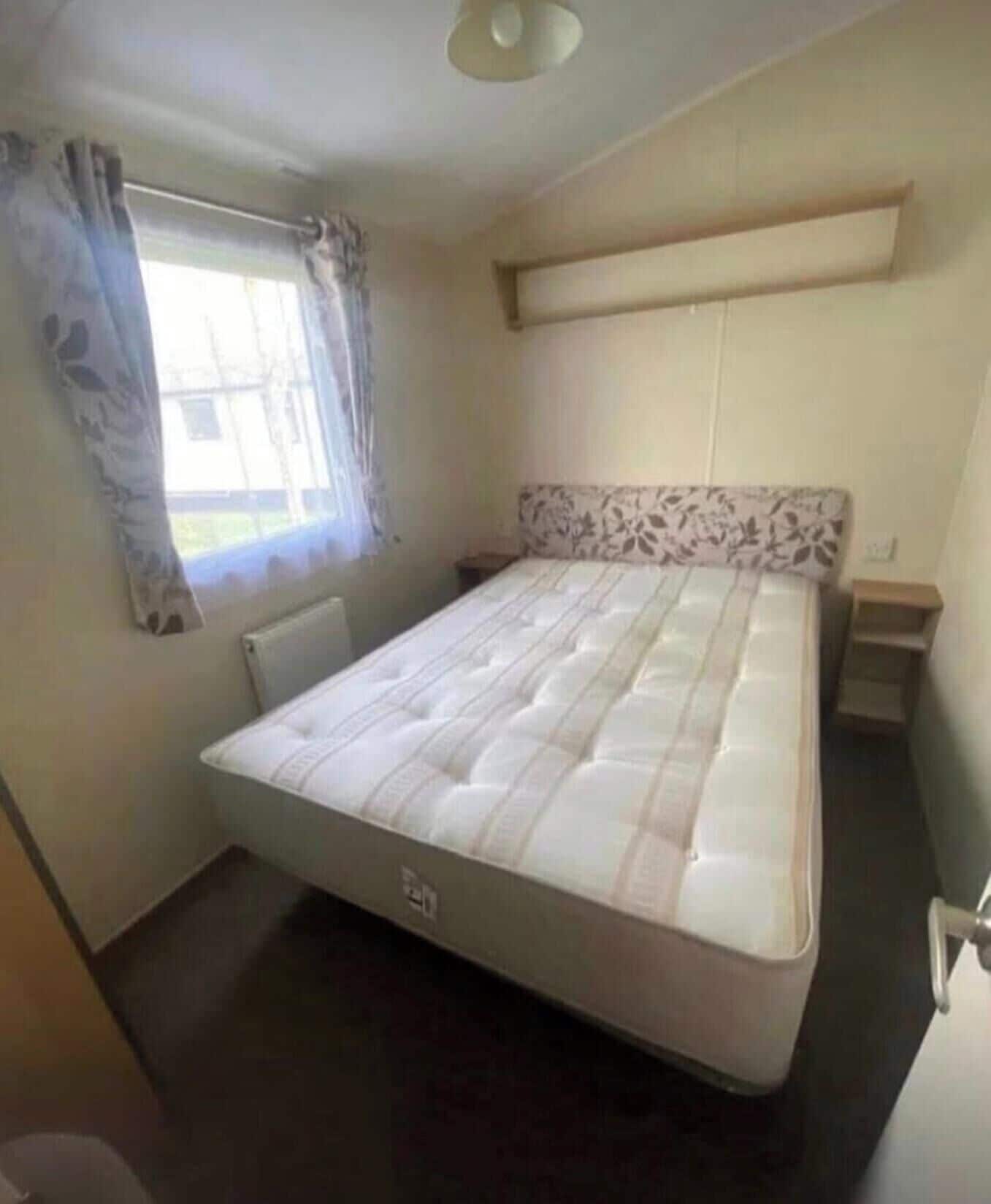 Een slaapkamer met een bed, een raam met gordijnen, een radiator en een hoofdbord met een bloemenmotief.