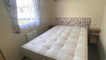 A bedroom with a bed, a window with curtains, a radiator, and a headboard with a floral pattern.