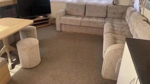 Ein möbliertes Wohnzimmer mit Sofa, Hocker und Fernseher.