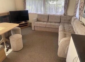 Ein möbliertes Wohnzimmer mit Sofa, Hocker und Fernseher.