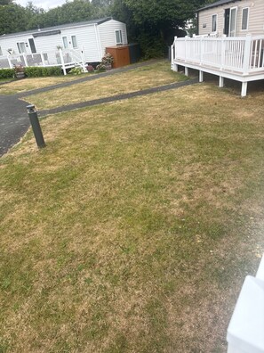 A grassy area with a white fence, a pathway, and a mobile home with a porch. - Holiday Home Sleeps 6 With Indoor Pool (Pwllheli)