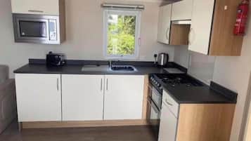 A compact kitchen with white cabinets, a microwave, a sink, a stove, and a window with a view of greenery.