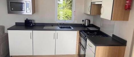 A compact kitchen with white cabinets, a microwave, a sink, a stove, and a window with a view of greenery.