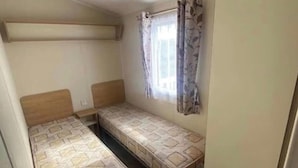 Ein kleines Zimmer mit zwei Einzelbetten, einem Deckenventilator und einem Fenster mit Vorhängen.