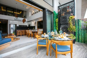 A modern dining area with a glass table, wooden chairs, and a kitchen in the background. - Romantic Zone 2BR Penthouse | Ocean Views & Pool (Puerto Vallarta)
