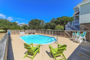 Ein Garten mit Schwimmbad, zwei grünen Adirondack-Stühlen und einer Holzterrasse.