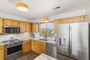 A modern kitchen with wooden cabinets, stainless steel appliances, a built-in oven, microwave, and refrigerator, and a window with blinds. - New Listing, Private Pool, Hot Tub, Walk to Beach, Dogs Welcome C0919 (Corolla)