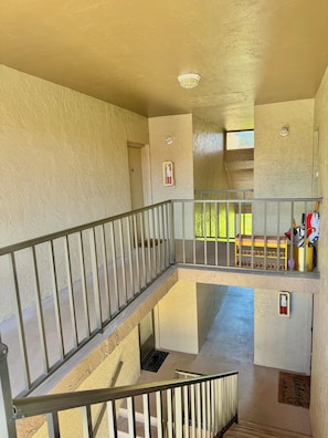 Ein mehrgeschossiges Interieur mit Metallgeländer, einer Bank und einer Tür zu einem Außenbereich.