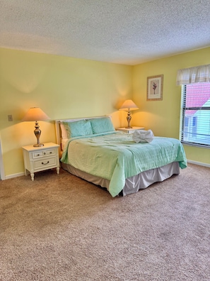 A bedroom with a bed, two bedside tables, a window with blinds, and a carpeted floor. - Steps from the white sand! Spacious 2-bedroom, 2-bath Pet Friendly 20 LBS (Indian Shores)