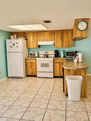 A compact kitchen with wooden cabinets, a refrigerator, a stove, a microwave, and a clock on the wall. - Steps from the white sand! Spacious 2-bedroom, 2-bath Pet Friendly 20 LBS (Indian Shores)