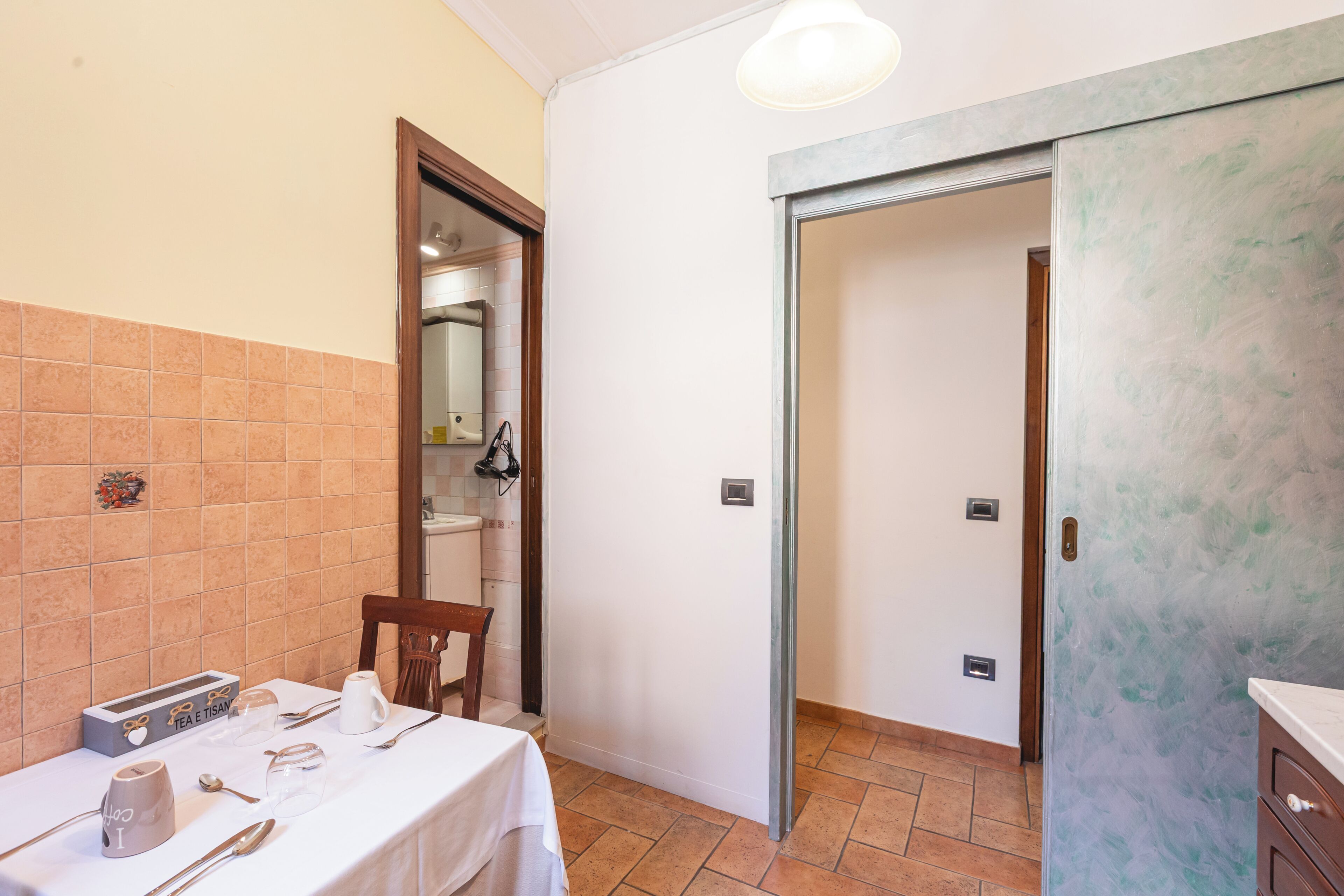 Una stanza con un tavolo da pranzo apparecchiato per quattro persone, una sedia, un armadio e una porta che dà su un'altra stanza.