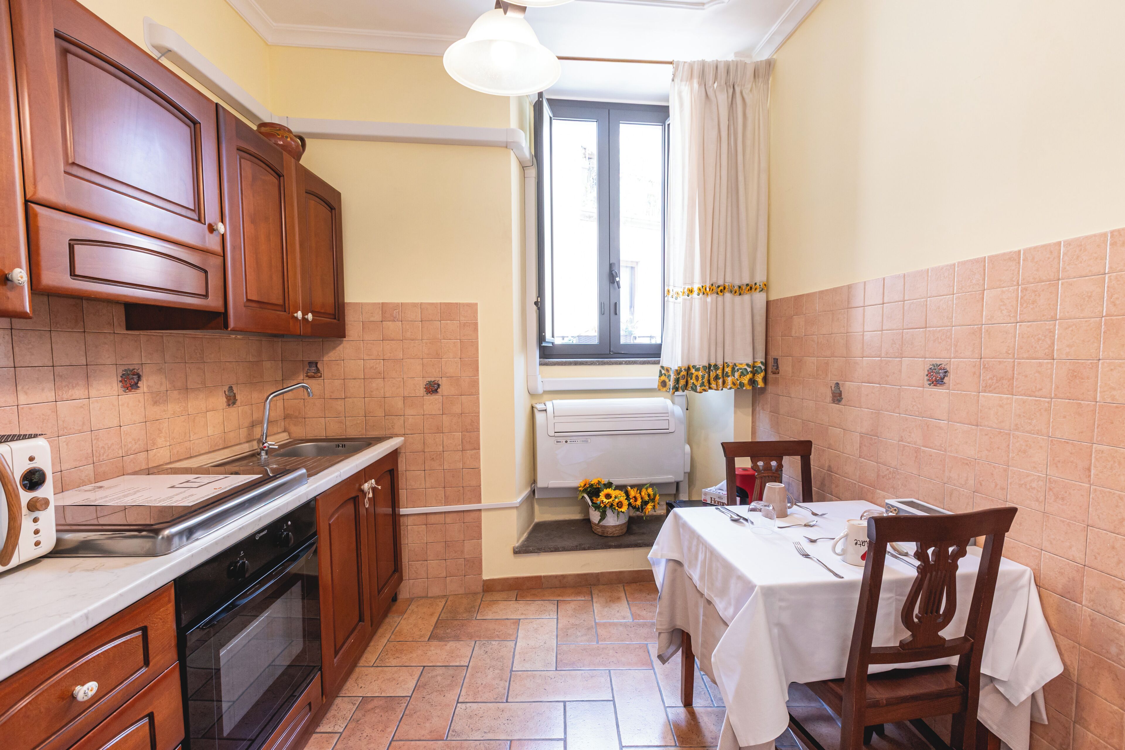 Una cucina compatta con mobili in legno, un forno a incasso e una zona pranzo con tavolo apparecchiato per due.