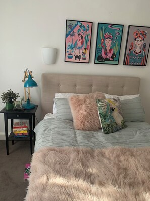 A bedroom with a bed, a nightstand with a lamp, a wall-mounted shelf, and three framed artworks. - Peaceful Hamptons spacious light filled charm. 5min walk shops, parks transport (Kooyong)