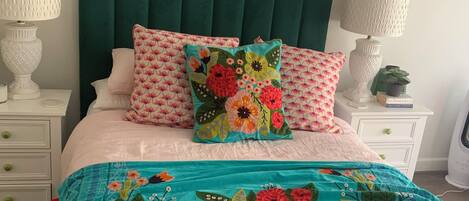 A bed with a teal floral bedspread, two white nightstands with lamps, and a green upholstered headboard.