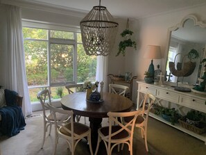 A dining area with a round table, white chairs, a hanging macrame light fixture, and a view of greenery outside. - Peaceful Hamptons spacious light filled charm. 5min walk shops, parks transport (Kooyong)