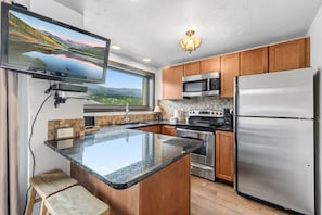 A modern kitchen with granite countertops, stainless steel appliances, wooden cabinets, and a large window offering a scenic view. - Ski-Inspired Mountain Getaway Steps from Peak 9 and Main Street! (Breckenridge)