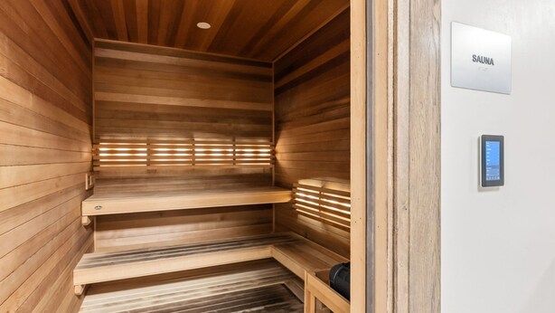 Sauna, jossa on puuseinät ja -lauteet, ohjauspaneeli sekä kyltti, joka kertoo tilan käyttötarkoituksen.