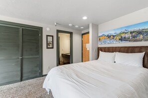 A hotel room with a bed, a painting of a mountain landscape, and a door leading to a bathroom. - Ski-Inspired Mountain Getaway Steps from Peak 9 and Main Street! (Breckenridge)