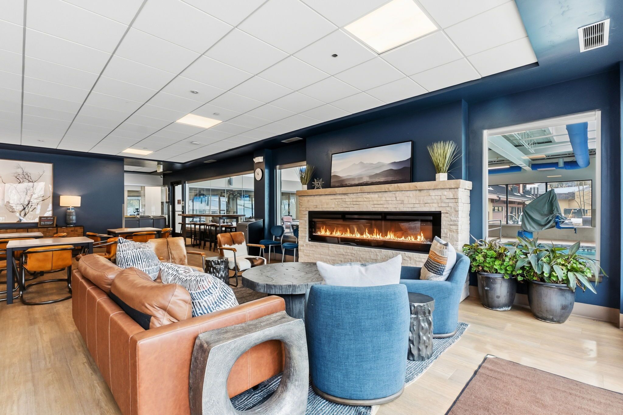 A modern lounge area with leather sofas, a stone fireplace, and potted plants.
