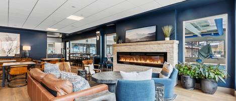 A modern lounge area with leather sofas, a stone fireplace, and potted plants.
