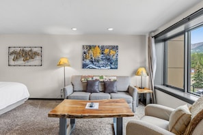 A hotel room with a bed, a sofa, a coffee table, two lamps, and a painting on the wall. - Ski-Inspired Mountain Getaway Steps from Peak 9 and Main Street! (Breckenridge)