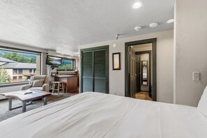 A hotel room with a bed, a desk, a chair, a television, and a view of the outside. - Ski-Inspired Mountain Getaway Steps from Peak 9 and Main Street! (Breckenridge)