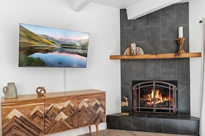 Ein modernes Wohnzimmer mit Kamin, einem Wandfernseher und einer Holzkommode.