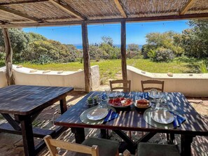 An outdoor dining area with tables and chairs, a view of the sea, and a thatched roof.