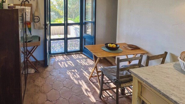 A small kitchen with a table and chairs, a refrigerator, and a door leading to an outdoor area. - Authentic Sardinian house 100 m from the sea (Carloforte)