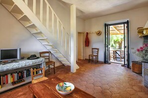 A room with a wooden floor, a staircase, a television, a bookshelf, and a door leading outside.