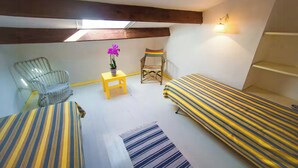 A small, cozy room with two beds, a chair, a small table, and a potted plant. - Authentic Sardinian house 100 m from the sea (Carloforte)