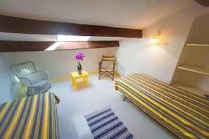 A small, cozy room with two beds, a chair, a small table, and a potted plant. - Authentic Sardinian house 100 m from the sea (Carloforte)