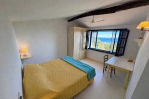A bedroom with a bed, a desk, and a view of the ocean. - Authentic Sardinian house 100 m from the sea (Carloforte)