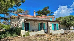 A traditional stone house with a tiled roof, blue shutters, and a stone pathway leading to the entrance. - Authentic Sardinian house 100 m from the sea (Carloforte)