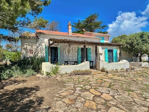 A traditional stone house with a tiled roof, blue shutters, and a stone pathway leading to the entrance. - Authentic Sardinian house 100 m from the sea (Carloforte)